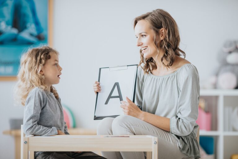 Logopeda pokazuje małej dziewczynce kartę z literą A podczas ćwiczeń wymowy w gabinecie terapeutycznym.